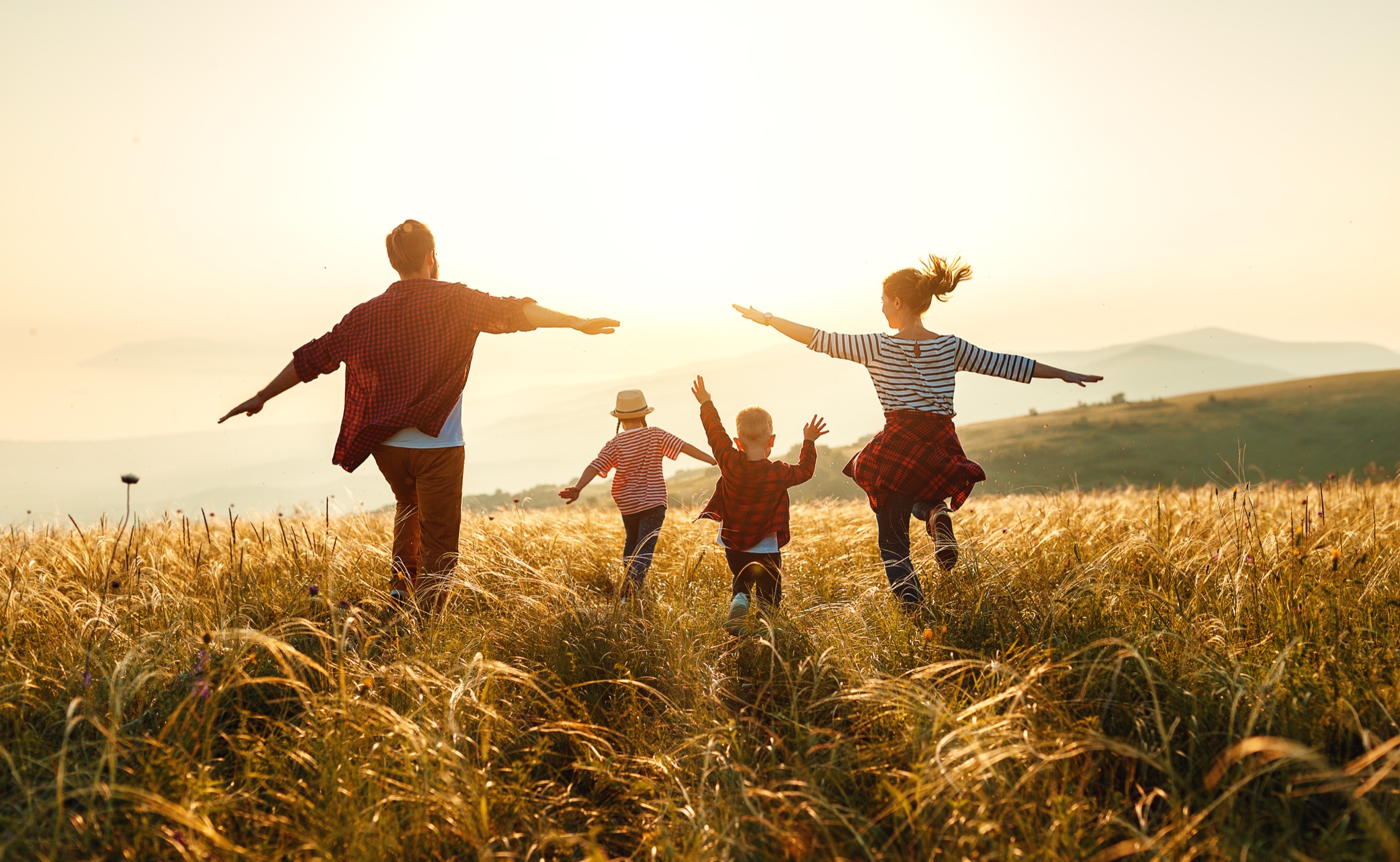 A family walking together through tall grass in open country at sunset.